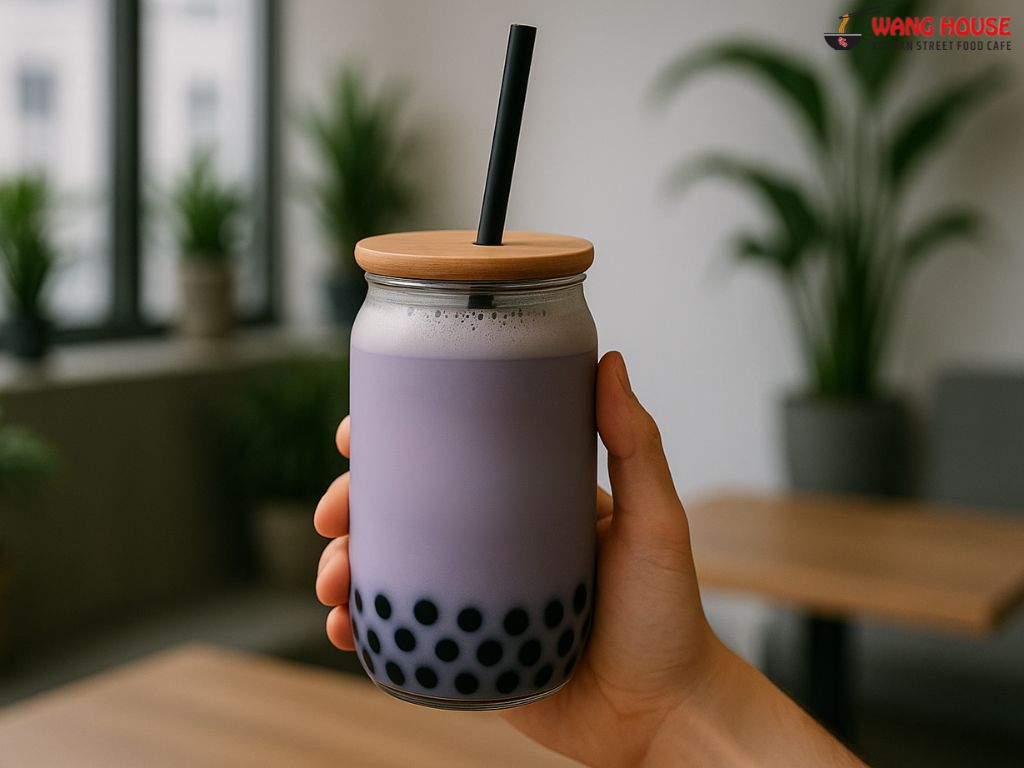 Nutty Taro boba tea in Delhi served at The Wang House, Laxmi Nagar – A stylish jar filled with light purple taro milk tea, topped with a creamy froth and black tapioca pearls at the bottom. The drink is presented in a clear glass jar with a golden lid and a black straw, set against a modern backdrop that highlights its smooth texture and nutty flavor profile, representing a must-try Korean-style boba experience in East Delhi.