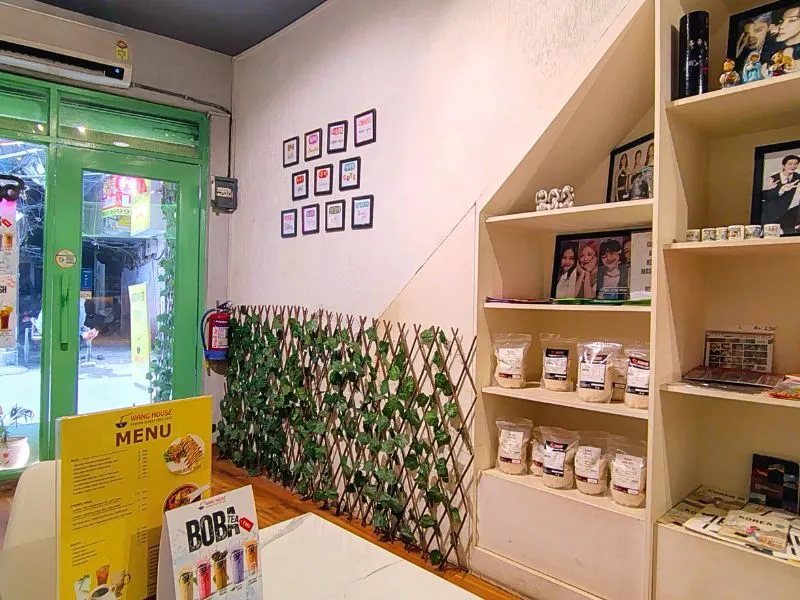 Interior of a cozy, bright Korean Theme Cafe, Warung House, showing shelves of merchandise, a vine lattice partition, and a green door