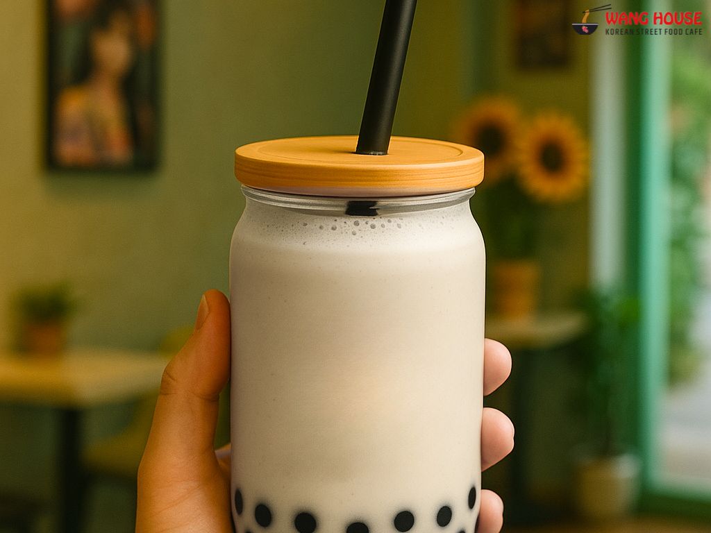 Cookies and Cream boba tea in Delhi from The Wang House, Laxmi Nagar – A creamy beige milk tea served in a sleek glass jar with a golden lid and black straw, featuring rich cookie flavor and chewy black tapioca pearls. The drink is styled on a soft-toned background, showcasing its indulgent texture and dessert-like appeal, perfect for boba lovers in East Delhi seeking a Korean-style twist.